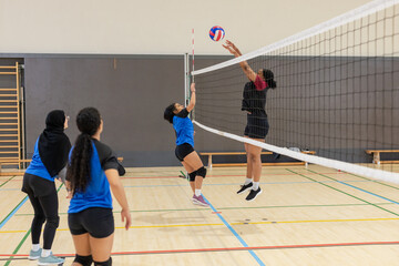 Diverse female volleyball team rallying at gym with ball, net, knee pads, benches, copy space