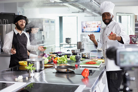 Diverse chefs filming a gourmet cooking demonstration on camera, teaching viewers to master complex recipes. Kitchen setup perfect for an engaging online course on professional food techniques.