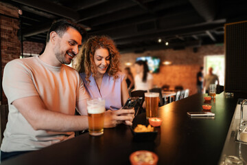Couple enjoying drinks and using smartphone at bar counter