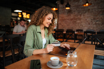 Young woman shopping online using laptop and credit card in cafe