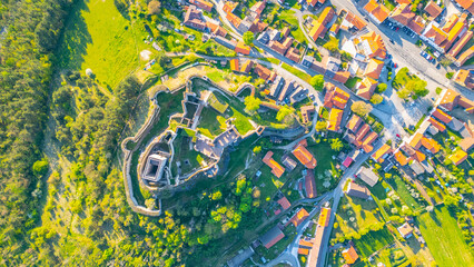 Aerial view captures the impressive Rabi Castle ruins nestled among the lush greenery, overlooking nearby village homes in Czechia. The landscape reveals historical architecture and scenic beauty.