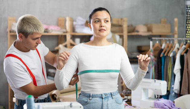 Attentive young male dressmaker measuring female client using tape in sewing workshop - Powered by Adobe