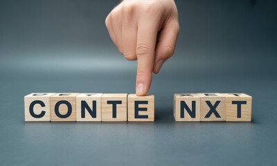 A hand's finger is positioned over the letter 'X' of the word "CONTENT NEXT" on light-brown wooden blocks, set against a muted gray background