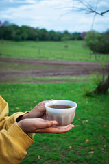 persona bebiendo té en el campo, manos jóvenes sosteniendo una taza de té caliento, bebida o infusión de hierbas.