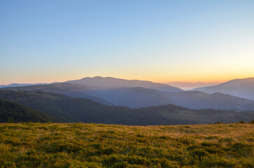 Vast mountain range stretches across the horizon under a clear, pale blue sky at sunrise. The...