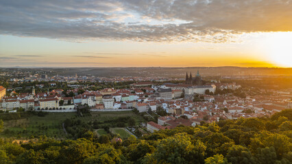 At sunrise, Prague Castle stands majestically against a vibrant sky, casting warm golden hues over the city's rooftops and lush greenery, capturing the essence of this historic site.