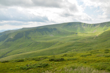 Panoramic view of vast, grassy mountain slopes under a partly cloudy sky. The rolling hills are a...