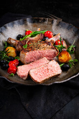 Traditional barbecue dry aged veal chop Mediterranean vegetable and fried potatoes served as close-up in a rustic cast iron frying pan