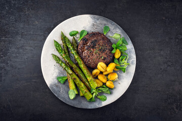 Grilled green asparagus with beef burger patty, gnocchi and fresh green salad served as top view on...