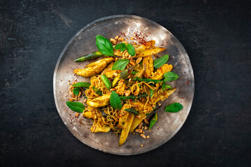 Stir fried Asian styly noodles with chicken filet, green and white asparagus with cashew nuts served as top view on a rustic design plate