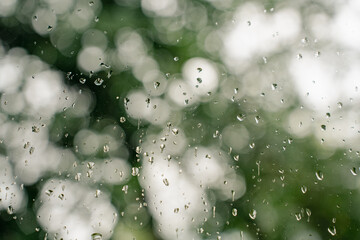 Raindrops on glass, blurred background of green and white bokeh in cloudy weather