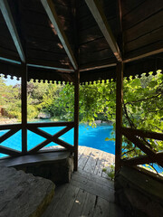 Fototapeta premium Cozy wooden gazebo surrounded by lush greenery, overlooking a serene blue swimming pool, creating a tranquil outdoor retreat for relaxation and leisure