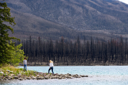 Mom with a teen boy are hiking at the shore of the lake among mountains and burnt forests after devastating wildfires. Lake Annette, Jasper national park, Canada.