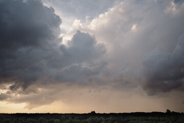 Dramatic thunderous sunset sky with dark huge rain clouds over green forest