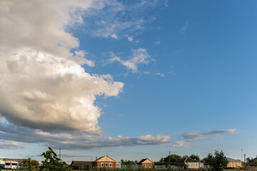 Large beautiful cumulus clouds in bright blue sky over rural area with houses, summer landscape