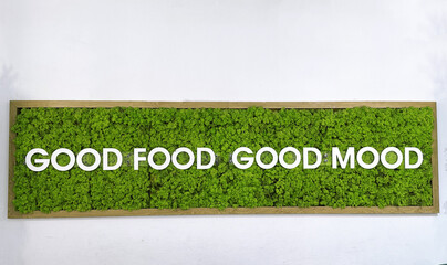 Green wall art featuring the phrase "Good Food Good Mood" in bold white letters, surrounded by vibrant moss, creating a lively and inviting atmosphere for dining spaces