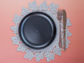 Top view empty black plate on round beige felt placemat with knife and fork on peach background