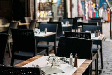 Modern cafe terrace with neatly arranged tables and chairs on a cobblestone street. Urban calm, quiet luxury, soft minimalism, refined casual dining