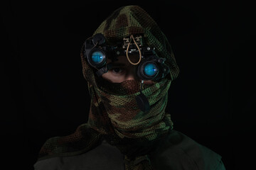 A special forces soldier in a camouflage net and modern night vision goggles, prepared for a covert...