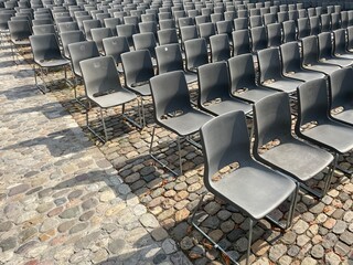 Rows of modern metal chairs arranged on a cobblestone square in front of historic European...