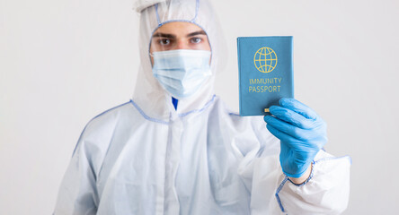 Medical specialist in protective biohazard costume showing coronavirus immunity passport on light studio background, selective focus. Covid-19 vaccination, protection against global virus concept