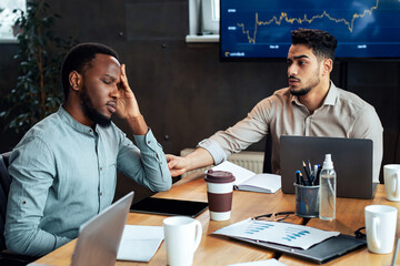 Sick young black male worker suffering from headache feeling migraine sitting at table in office...