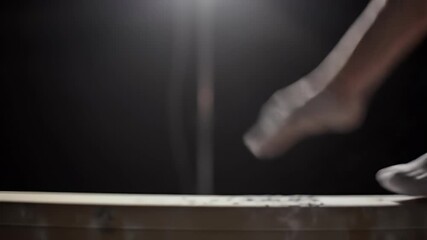 A dancer's bare feet in motion, kicking up dust as they land on a wooden surface under dramatic spotlighting.