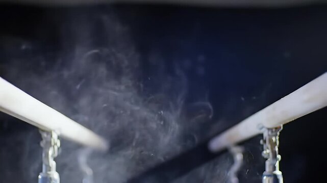Close-up of parallel bars with chalk dust suspended in the air against a dark background, highlighting athletic preparation.