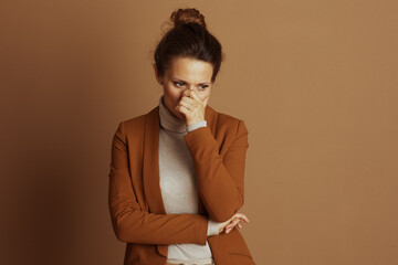 A concerned businesswoman, hand covering her mouth and nose, looks downwards with a pensive...