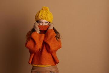 Playful woman in knit hat and oversized orange turtleneck pulls sweater collar up with gloved...