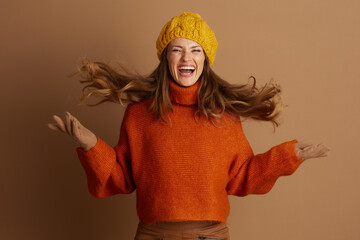 Young woman, flowing light brown hair, yellow beanie, orange turtleneck, laughs energetically, arms...