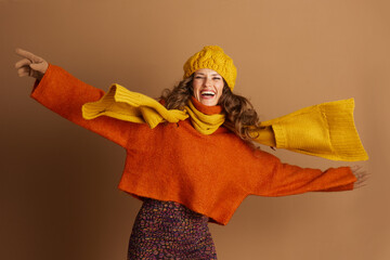 A joyful young woman with curly brown hair wears a vibrant orange sweater, yellow knit scarf, and...