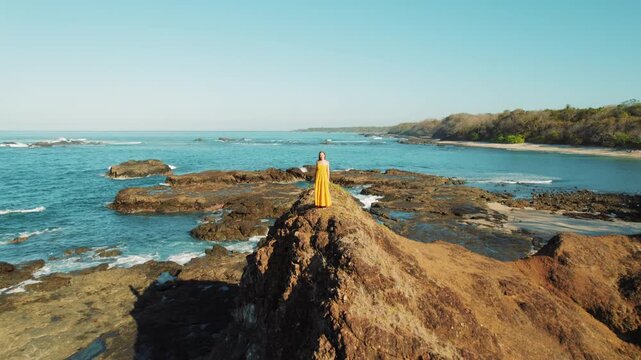 Woman in yellow dress overlooking rocky coastal beach San Juanillo in Costa Rica