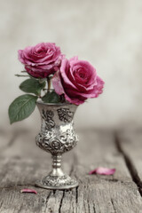 A wooden tabletop scene featuring an elegant vase with a few roses inside