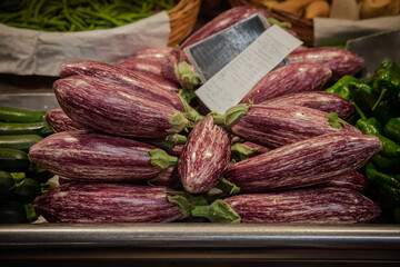 Close view of purple and white striped graffiti eggplants, also called Sicilian eggplants, stacked at a market stall beside other vegetables, highlighting fresh produce and Mediterranean varieties.