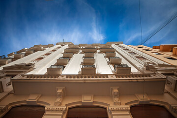 Obraz premium Upward view of a residential facade in Valencia old town, showing balconies, classical details and small terraces. The composition emphasizes housing and property character in the historic center.