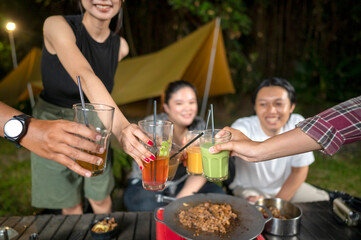 Indonesian southeast asian people relaxing together outdoors and enjoying refreshing drinks while cooking sliced beef on a grill pan. The scene of the lifestyle of enjoying food in a natural setting