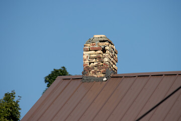 A brick chimney on the metal roof with blue sky