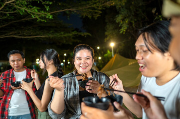 Indonesian southeast asian people are enjoying a meal, using chopsticks to serve themselves a barbecue meal from small black bowls. The scene of the lifestyle of enjoying food in a natural setting