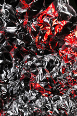Close up of crumpled aluminum foil with shiny silver surface and dramatic red highlights. Abstract...