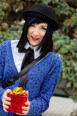 Young Woman Holding Red Gift Box in Retro Outfit Smiling Outdoors, individuality femininity concepts