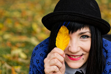 Woman Smiles with Yellow Leaf Near Eye in Autumn Park, individuality femininity concepts