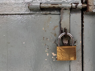  A close-up view of a large, shiny golden padlock, securely fastened on a heavy, old, and rusty...