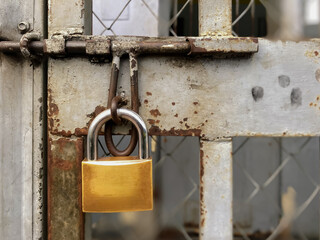  A close-up view of a large, shiny golden padlock, securely fastened on a heavy, old, and rusty...