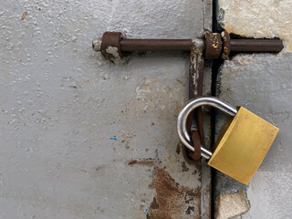 A close-up view of a large, shiny golden padlock, securely fastened on a heavy, old, and rusty...