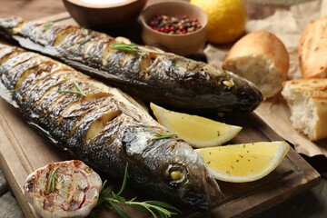 Tasty roasted seabass fish served with bread, rosemary and lemon on wooden table, closeup. Homemade seafood dish