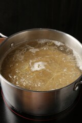 Fresh tagliatelle pasta boiling in pot with water on electric stove, closeup