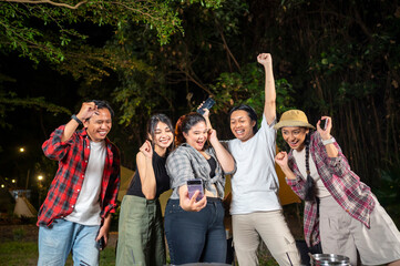 Obraz premium Indonesian southeast asian people enjoying a camping at night, using their cellphones to capture moments and share experiences. The scene of the lifestyle of enjoying camping in a natural setting