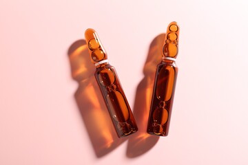 Glass ampoules with liquid on pink background, flat lay