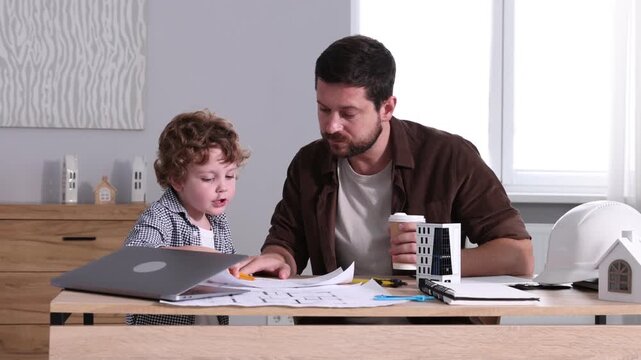 Choice of profession. Father and his son exploring engineering drawings at table indoors, camera moving in